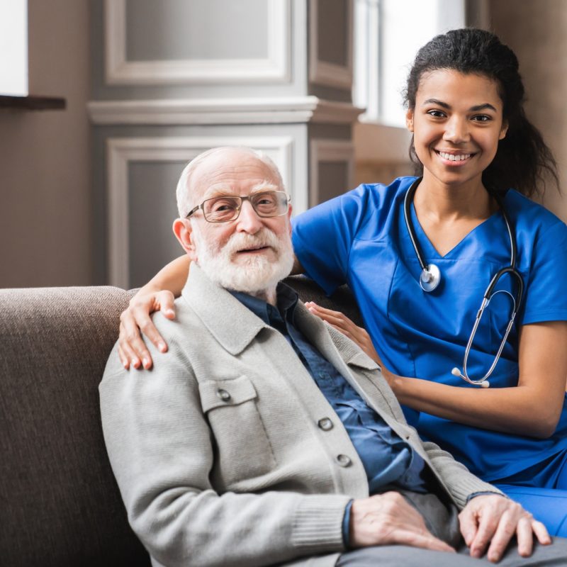 Front view portrait of caring afro nurse taking care of an elderly caucasian man grandfather Front view portrait of caring afro nurse taking care of an elderly caucasian man grandfather