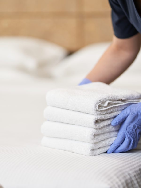 Housemaid making bed in hotel room while folding towels