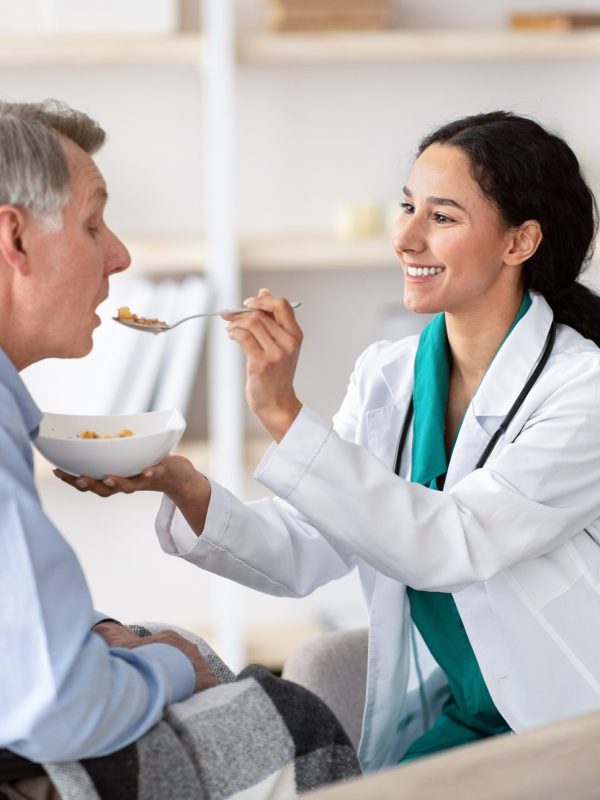Medical assistance for elderly people with disabilities. Nurse feeding senior handicapped man in