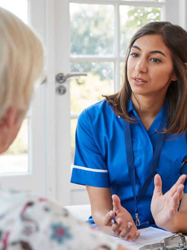 Senior woman talking to young care nurse on home visit